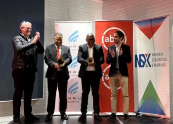 Five men in suits on a stage clap, with banners for the Namibia Securities Exchange and other logos in the background.