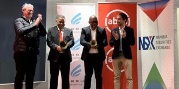 Five men in suits on a stage clap, with banners for the Namibia Securities Exchange and other logos in the background.