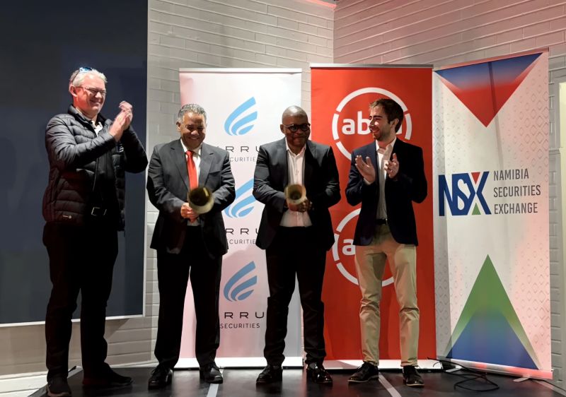 Five men in suits on a stage clap, with banners for the Namibia Securities Exchange and other logos in the background.