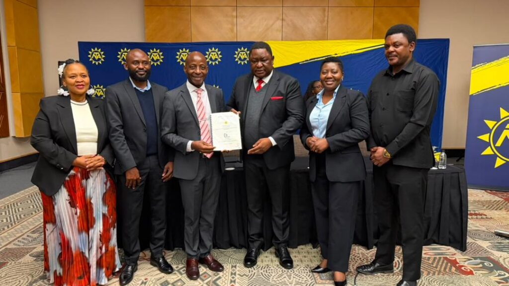 WhatsApp Image 2026-08-10 at 35809 PM - The Brief | Namibia's Leading Business & Financial News Six professionals in business attire posing for a photo at a ceremony, with a man in the center holding a certificate.