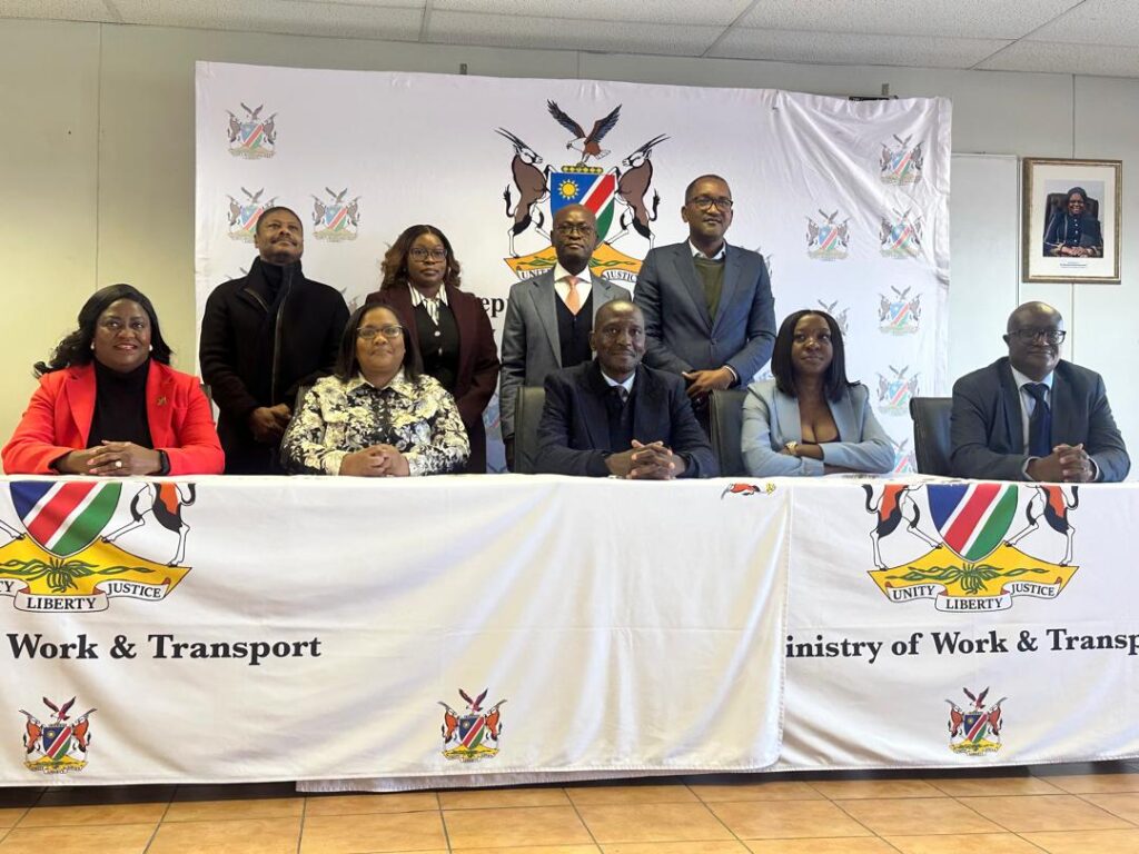 WhatsApp Image 2026-08-10 at 52341 PM - The Brief | Namibia's Leading Business & Financial News Eight professionals sit and stand behind a long table at a Ministry of Work & Transport event, with a banner displaying the ministry crest behind them.
