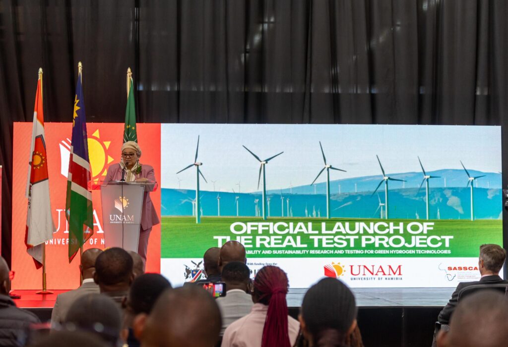 WhatsApp Image 2026-08-11 at 95538 AM - The Brief | Namibia's Leading Business & Financial News Speaker at a podium giving a speech at an official launch event, with flags and a banner that reads 'Official Launch of the Real Test Project' behind her.