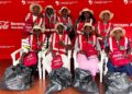 Group of Coca-Cola Namibia volunteers in red vests and hats pose for photo with trash bags at a Beverages Africa event backdrop