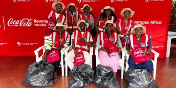 Group of Coca-Cola Namibia volunteers in red vests and hats pose for photo with trash bags at a Beverages Africa event backdrop