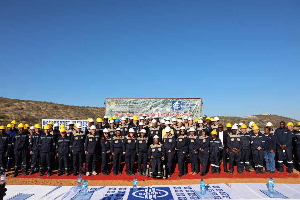 MMR Group Photo - The Brief | Namibia's Leading Business & Financial News Group photo of dozens of workers in navy and tan uniforms wearing hard hats on a red carpet at a mining site, with a banner in the background reading Sinomine Tsumeb Multi-Metal Recovery.