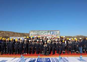 MMR Group Photo - The Brief | Namibia's Leading Business & Financial News Group photo of dozens of workers in navy and tan uniforms wearing hard hats on a red carpet at a mining site, with a banner in the background reading Sinomine Tsumeb Multi-Metal Recovery.