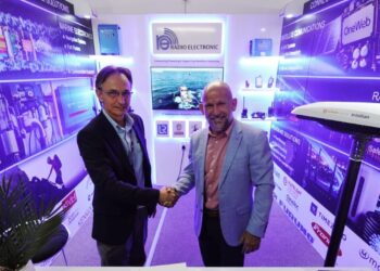 Two men in business attire shake hands at a tech expo booth with blue-lit banners and branding.