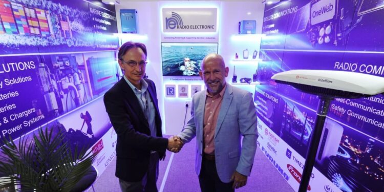 Two men in business attire shake hands at a tech expo booth with blue-lit banners and branding.