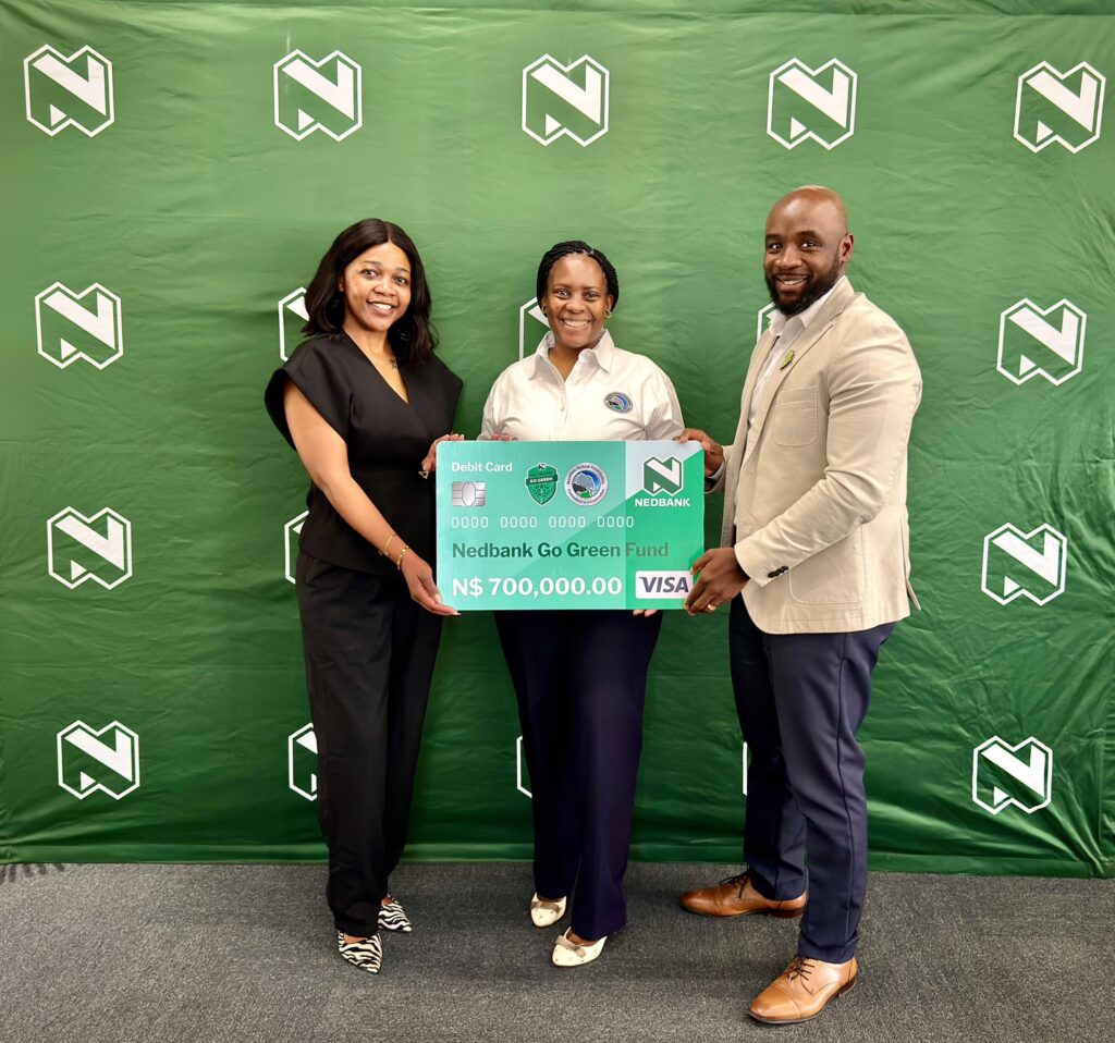 WhatsApp Image 2026-08-11 at 43049 PM - The Brief | Namibia's Leading Business & Financial News Three people pose with a large Nedbank Go Green debit card prop in front of a green backdrop featuring white logos, smiling for the photo.