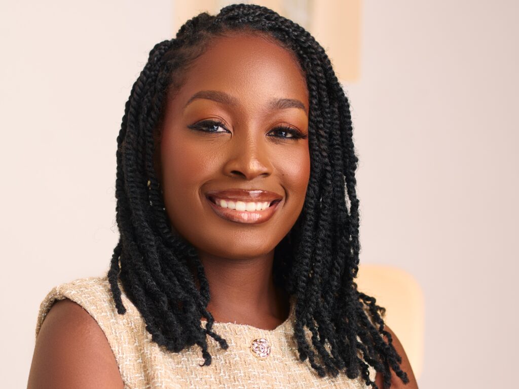 Rejoice Amutenya - The Brief | Namibia's Leading Business & Financial News Close-up portrait of a smiling Black woman with long black braids and a beige textured top against a light background.