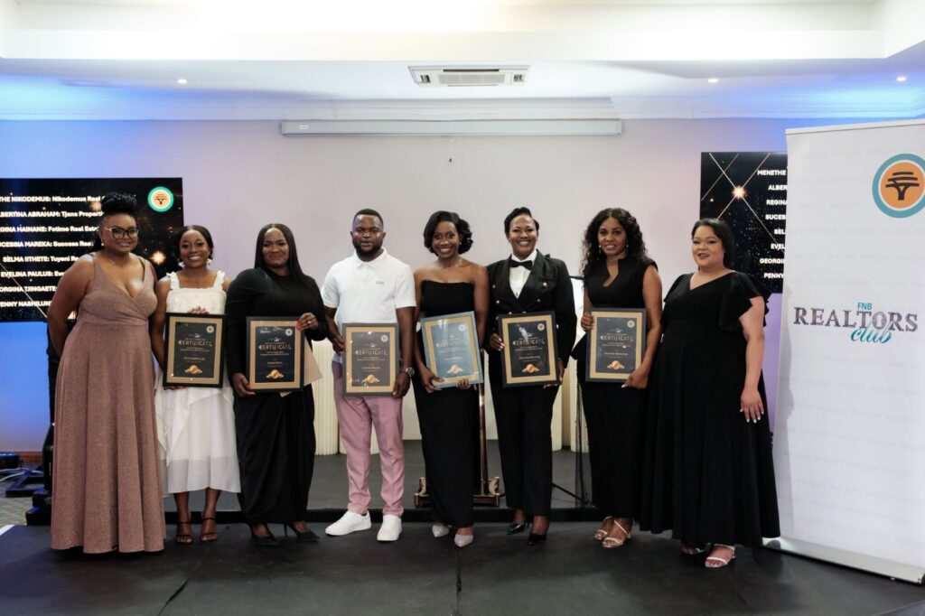 Group of eight people on a stage holding certificates at an awards event, smiling for the camera.