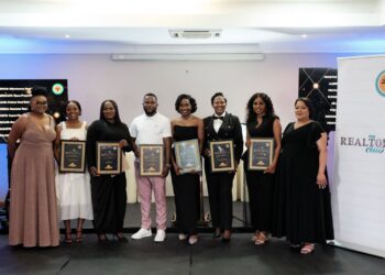 Group of eight people on a stage holding certificates at an awards event, smiling for the camera.