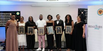 Group of eight people on a stage holding certificates at an awards event, smiling for the camera.