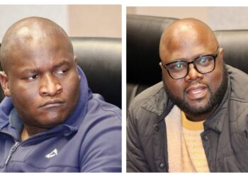 MixCollage-13-Aug-2026-04-20-PM-1386 - The Brief | Namibia's Leading Business & Financial News Two men seated on a couch side by side; left: bald man in a blue zip-up jacket looking to the left, right: man with glasses and beard wearing a tan sweater and dark jacket, looking at the camera