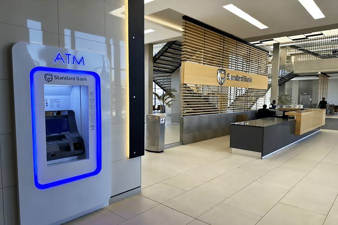 STANDARD BANK ATM - The Brief | Namibia's Leading Business & Financial News Indoor Standard Bank lobby with a blue-lit ATM on the left and a service desk visible in the background.