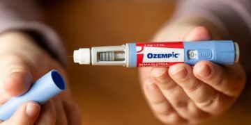 Close-up of a hand preparing an Ozempic diabetes injectable pen, with the blue cap removed and the needle exposed.