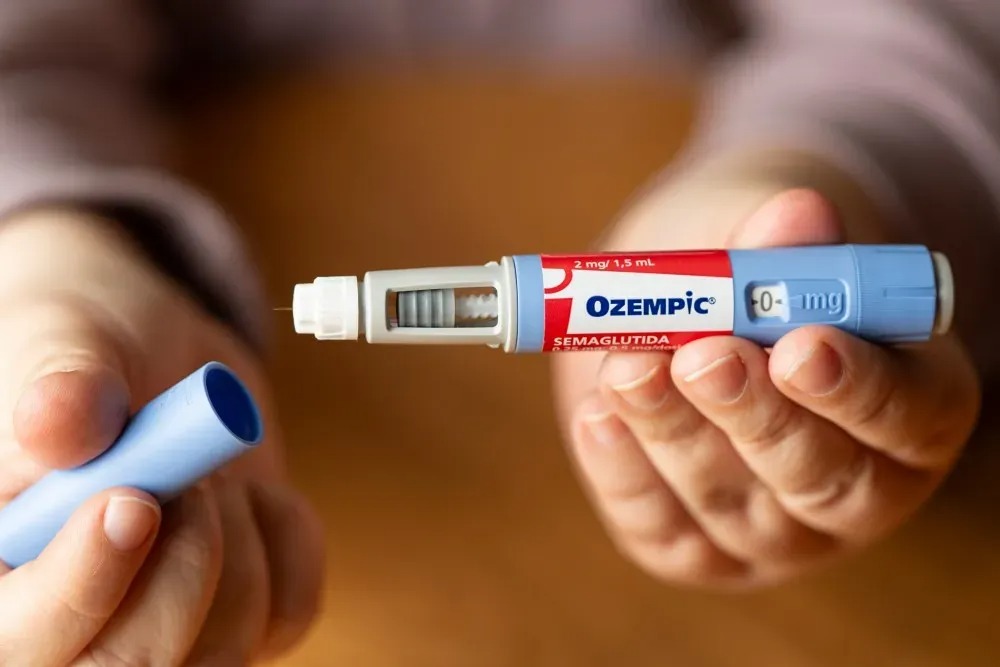 Close-up of a hand preparing an Ozempic diabetes injectable pen, with the blue cap removed and the needle exposed.