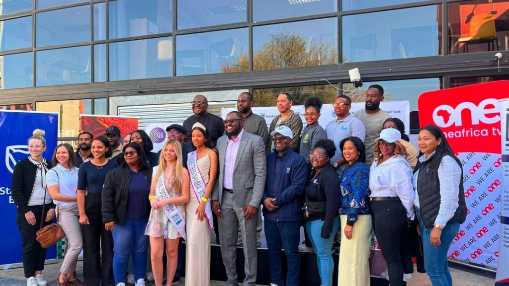 WhatsApp Image 2026-08-16 at 40853 PM - The Brief | Namibia's Leading Business & Financial News Diverse group of people posing outside a glass-front building for a community event, several wearing sashes and smiling at the camera.