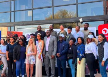 WhatsApp Image 2026-08-16 at 40853 PM - The Brief | Namibia's Leading Business & Financial News Diverse group of people posing outside a glass-front building for a community event, several wearing sashes and smiling at the camera.
