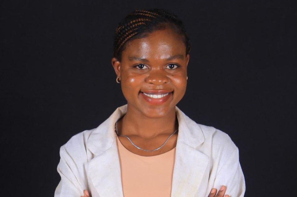 Apolonia H Ndakolo - The Brief | Namibia's Leading Business & Financial News Smiling woman in a light blazer over a peach top, posing with arms crossed against a dark background.