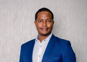 Professional portrait of a man in a blue blazer and white shirt, smiling slightly, facing the camera against a neutral textured background.