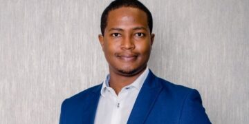 Professional portrait of a man in a blue blazer and white shirt, smiling slightly, facing the camera against a neutral textured background.