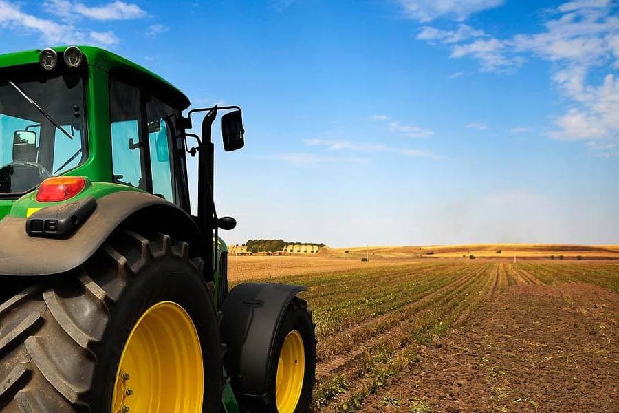 Green tractor with large yellow wheels on a flat farm field under a bright blue sky