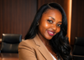 Smiling Black woman in a tan blazer posing in a conference room with dark wood panels behind her.