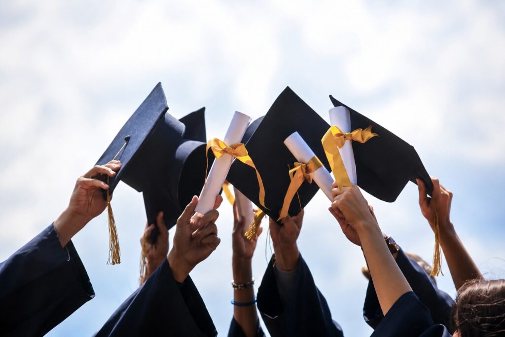 GRADUATE2 - The Brief | Namibia's Leading Business & Financial News Group of graduates in navy gowns throwing their black mortarboards with gold tassels into the air against a blue sky