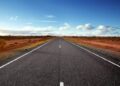 Straight highway through a desert landscape under a blue sky with a few clouds.