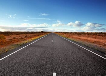 Straight highway through a desert landscape under a blue sky with a few clouds.