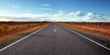 Straight highway through a desert landscape under a blue sky with a few clouds.