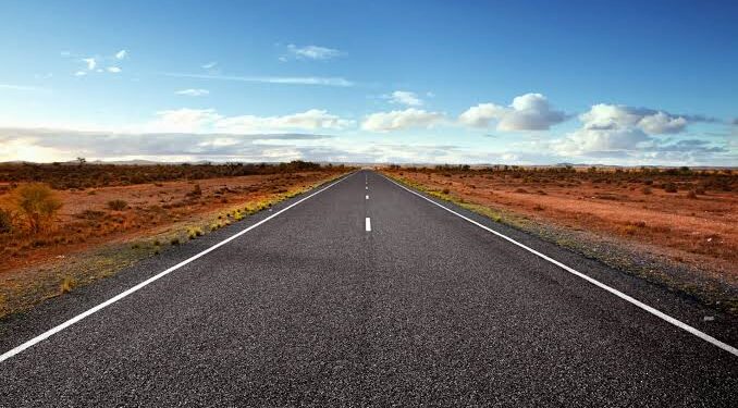 Straight highway through a desert landscape under a blue sky with a few clouds.