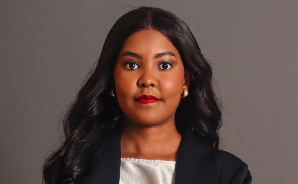 Portrait of a woman with long black hair, wearing a black blazer and white top, looking at the camera on a gray studio backdrop