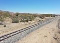Desert landscape with a single set of railroad tracks curving into the distance under a clear blue sky.