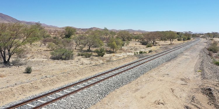 Desert landscape with a single set of railroad tracks curving into the distance under a clear blue sky.