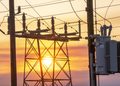 Electrical substation with transformers and hanging wires silhouetted against a sunset sky.