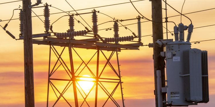 Electrical substation with transformers and hanging wires silhouetted against a sunset sky.