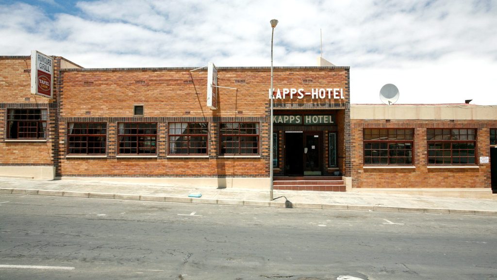 Kapps Hotel - The Brief | Namibia's Leading Business & Financial News Brick hotel building with a sign reading'KAPPS-HOTEL' on a sunny street, sidewalk in front and several wide windows on either side of the entrance.