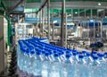 Row of blue-capped bottled water on a conveyor belt in a bottling plant.