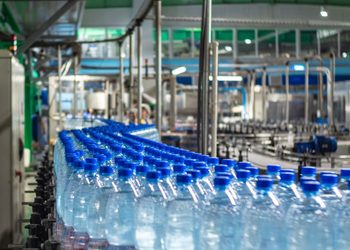 Row of blue-capped bottled water on a conveyor belt in a bottling plant.