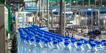 Row of blue-capped bottled water on a conveyor belt in a bottling plant.