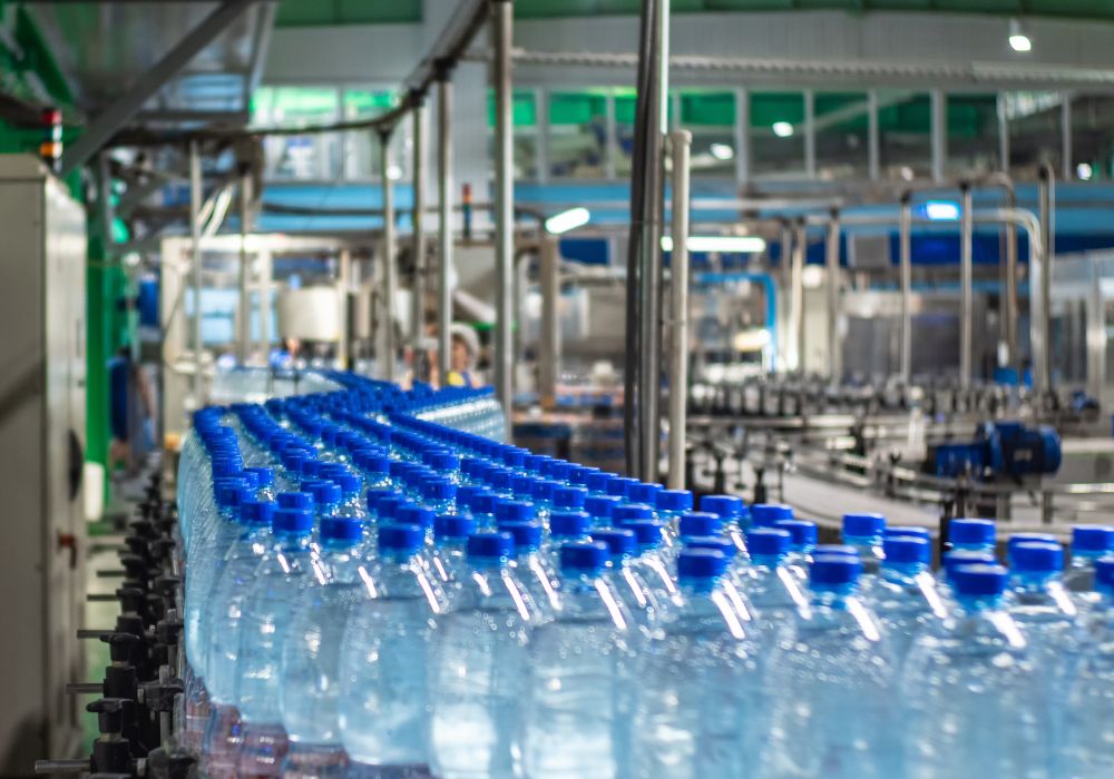 plastic bottles - The Brief | Namibia's Leading Business & Financial News Row of blue-capped bottled water on a conveyor belt in a bottling plant.