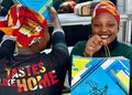 Two women wearing colorful headwraps smile as they hold bright Galito's chicken bags, with one wearing a shirt that reads 'TASTES LIKE HOME.'