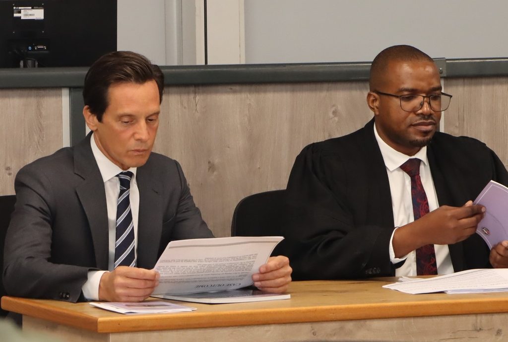 WhatsApp Image 2026-08-28 at 114028 AM - The Brief | Namibia's Leading Business & Financial News Two men in formal attire sit at a wooden table, reading papers in a formal meeting or hearing.