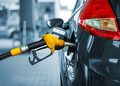 Close-up of a yellow fuel nozzle inserted into the fuel port of a dark-colored car at a gas station, ready for refueling.