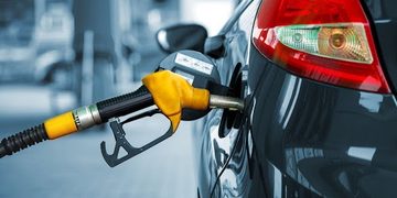 Close-up of a yellow fuel nozzle inserted into the fuel port of a dark-colored car at a gas station, ready for refueling.