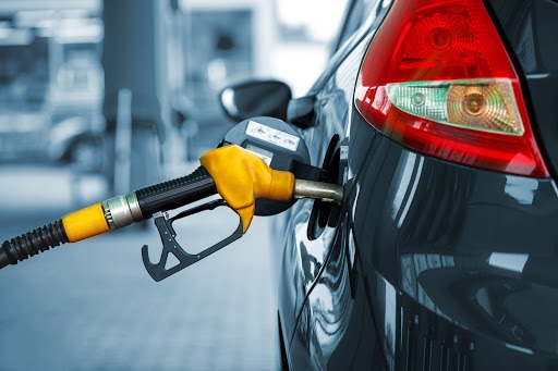 Close-up of a yellow fuel nozzle inserted into the fuel port of a dark-colored car at a gas station, ready for refueling.