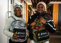 WhatsApp Image 2026-09-01 at 14734 PM - The Brief | Namibia's Leading Business & Financial News Two smiling women indoors, each wearing a colorful patterned backpack with Unmatched Potential branding and Capricorn Foundation logos visible on the pouches.