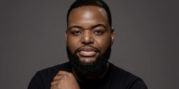 Head-and-shoulders portrait of a man with a beard in a black shirt against a gray backdrop.